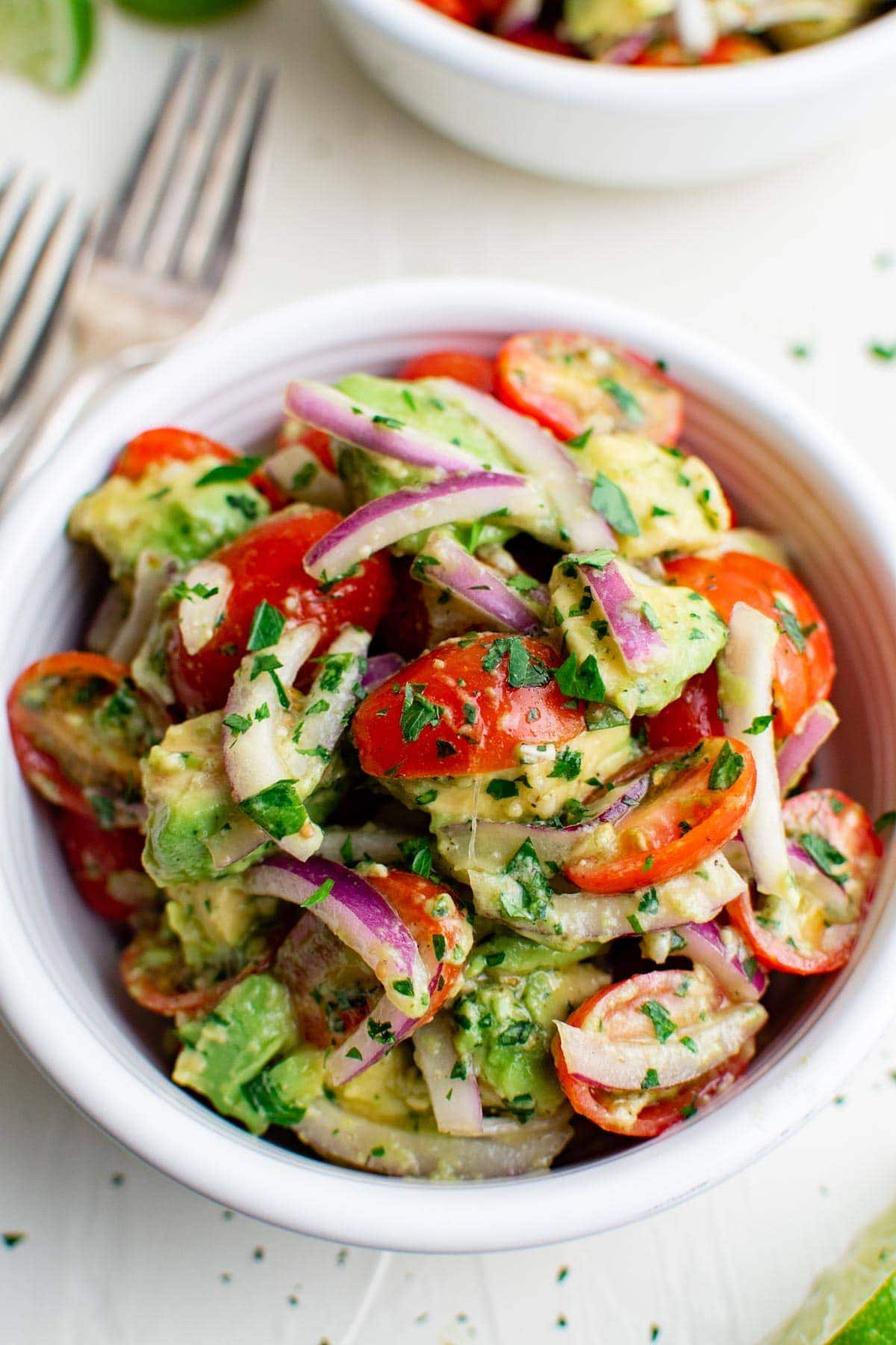 tomatoes, avocados, red onions, parsley in a white bowl, 2 forks