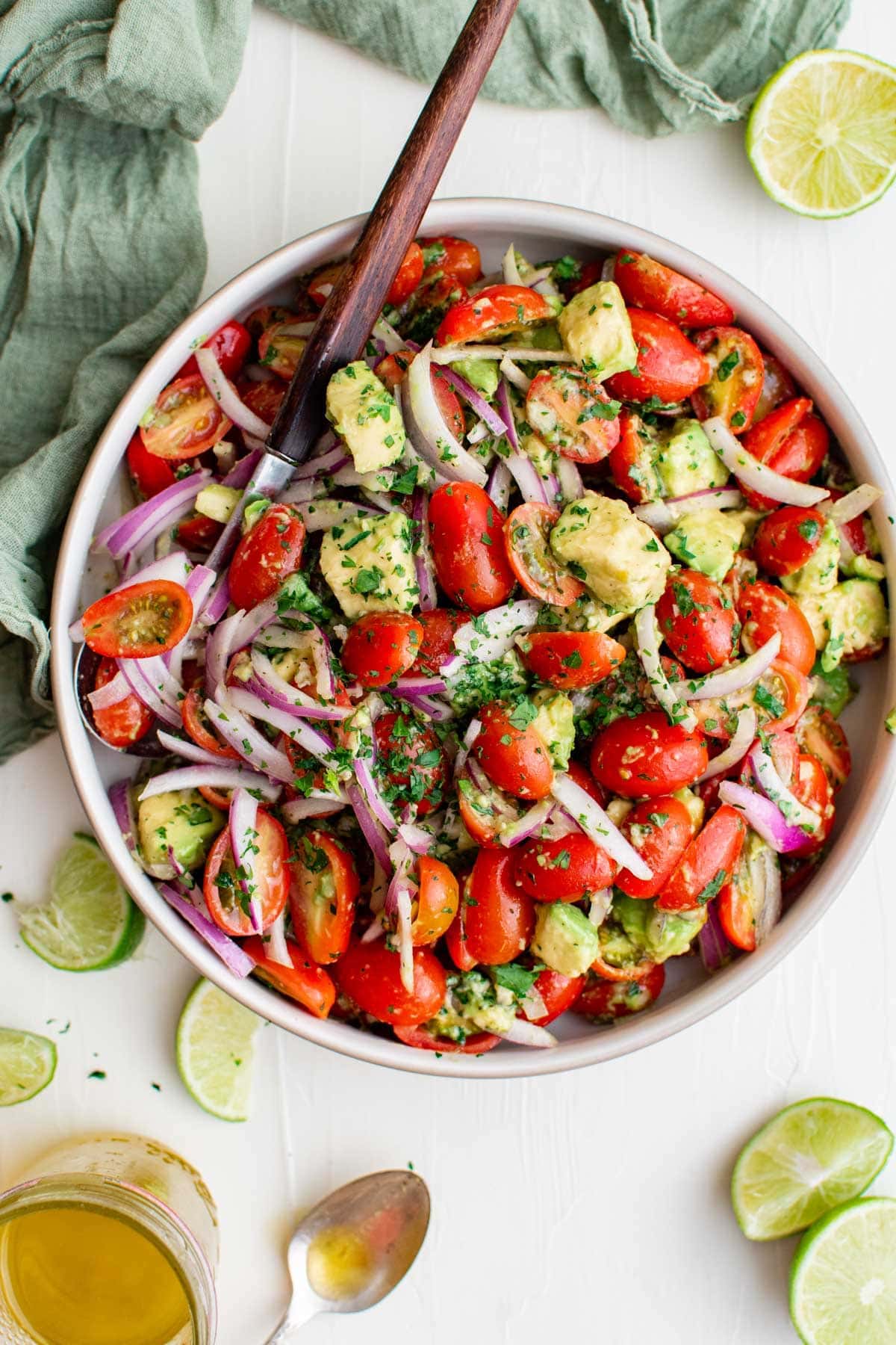 Tomato avocado salad served in a big bowl with a wooden spoon on the side