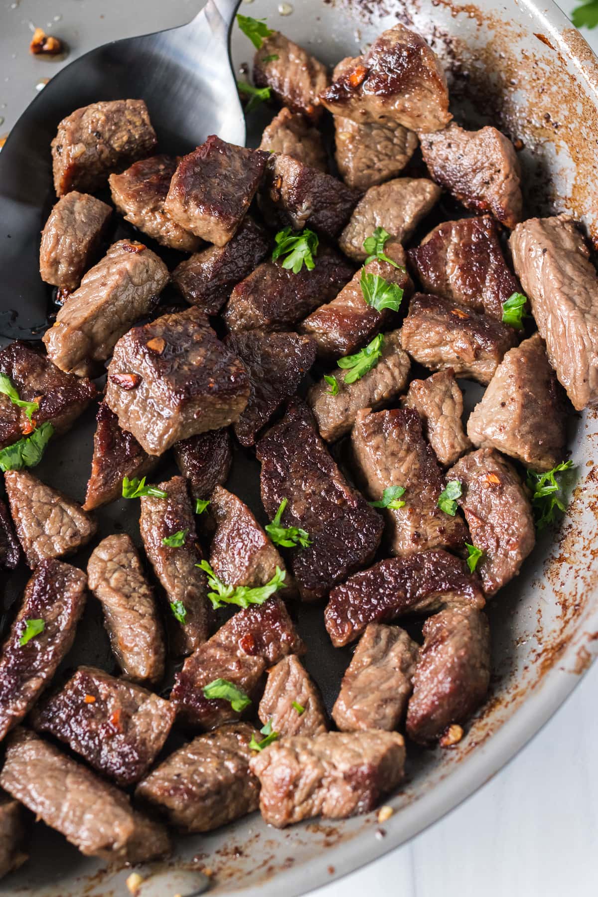 steak bites in a skillet being scooped with a spoon