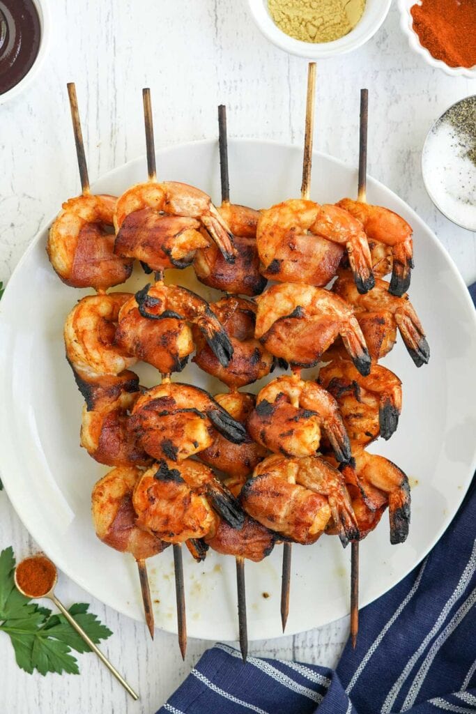 shrimp wrapped in bacon and threaded on skewers, white plates, cups of sauces