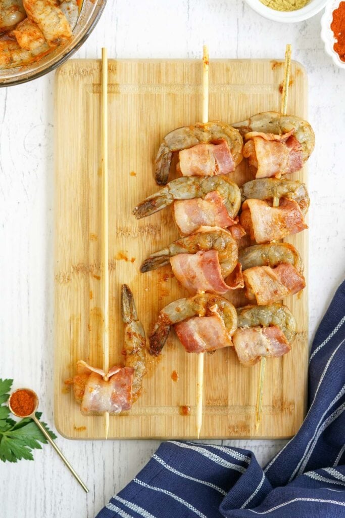 cutting board, shrimp threaded on wooden skewers, wrapped in bacin