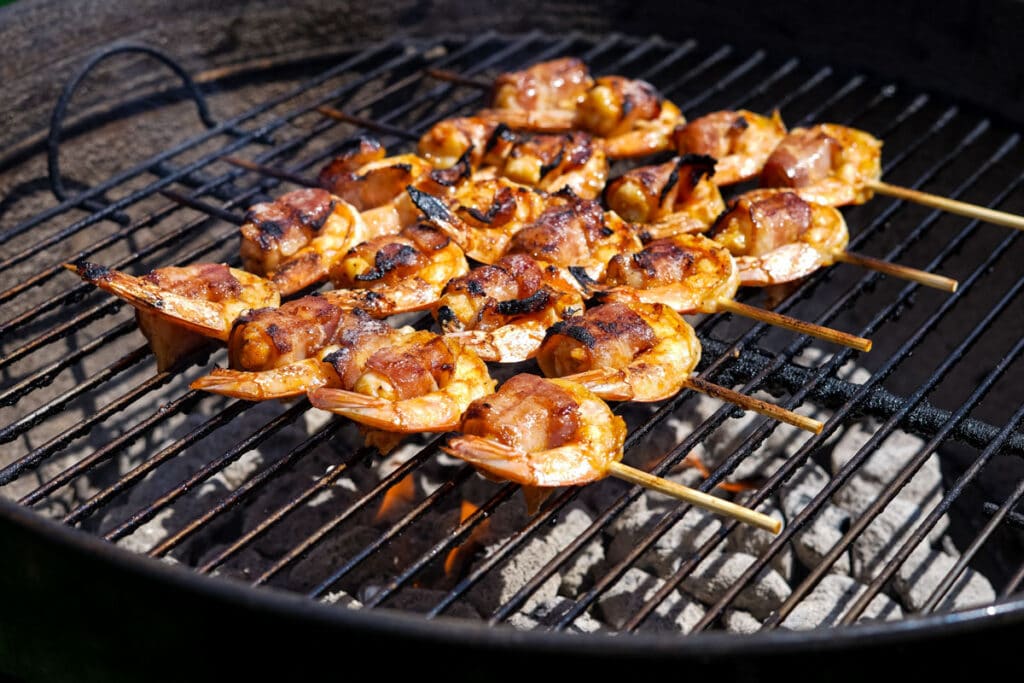 shrimp wrapped in bacon, threaded on skewers, on a grill