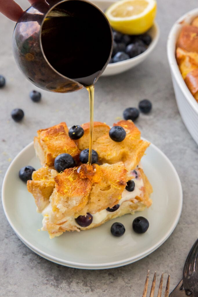 slice of blueberry french toast casserole, pitcher pouring on maple syrup