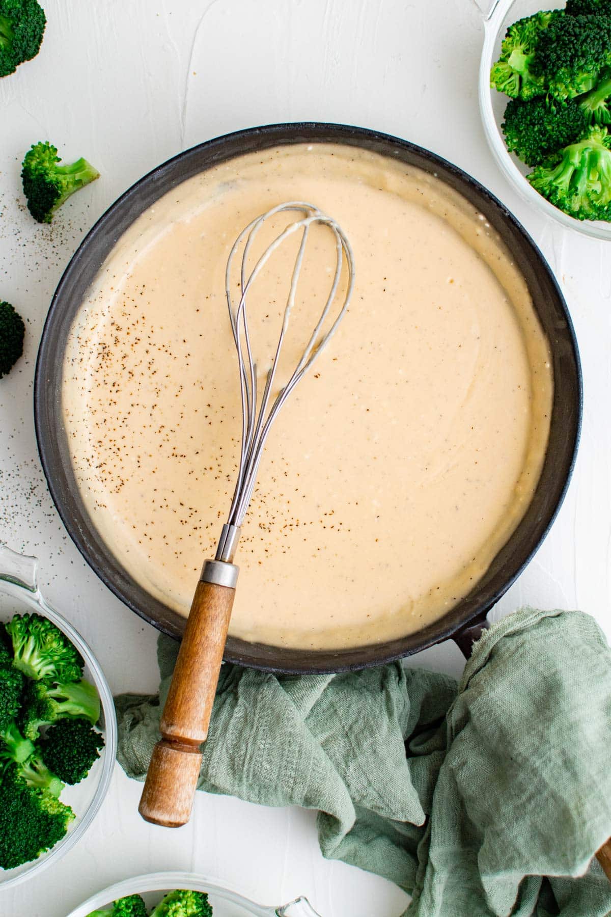 skillet with cheese sauce, whisk, broccoli, green towel