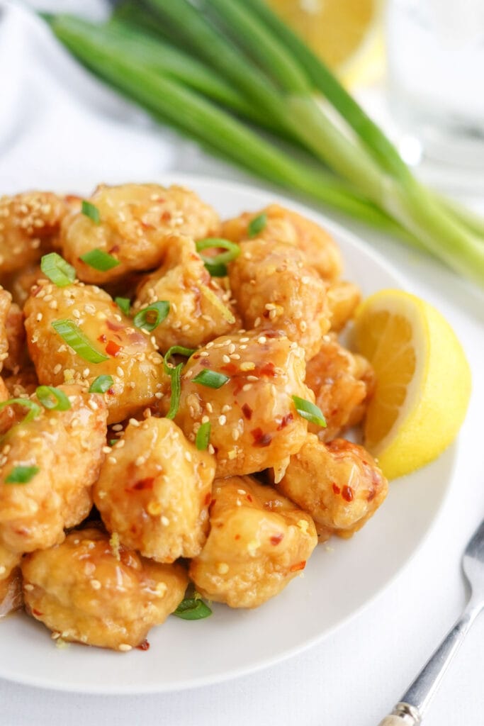 chinese lemon chicken with lemon sauce on a white plate with lemon and green onions and sesame seeds