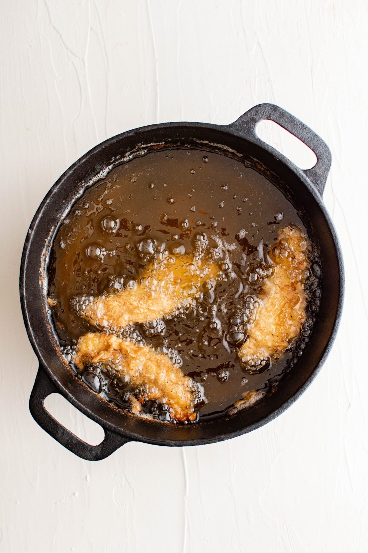 breaded chicken tender frying in oil in a cast iron skillet