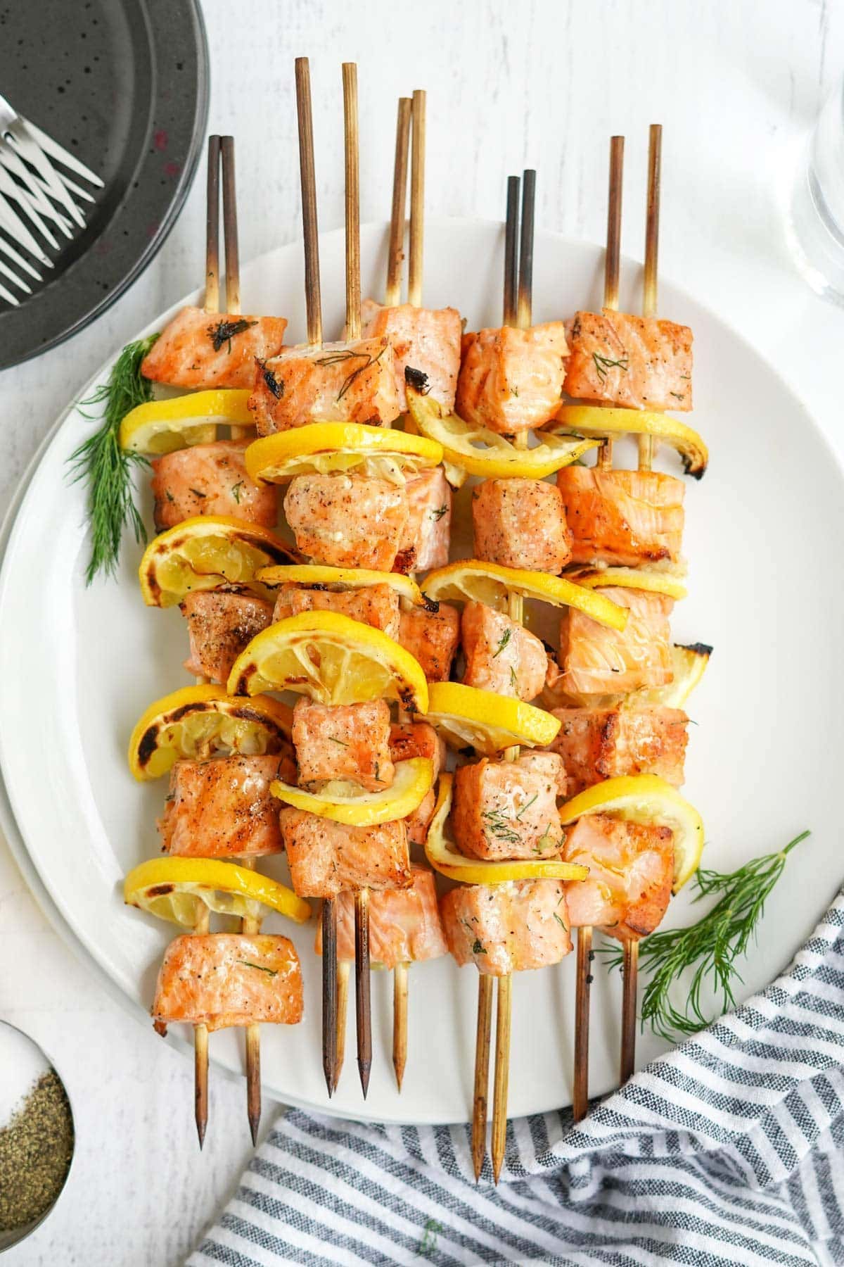 grilled salmon on skewers on a white plat with black and white striped napkin