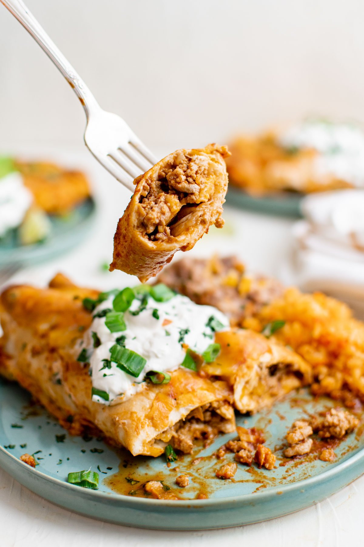 ground turkey enchiladas on a blue plate, a fork sour cream