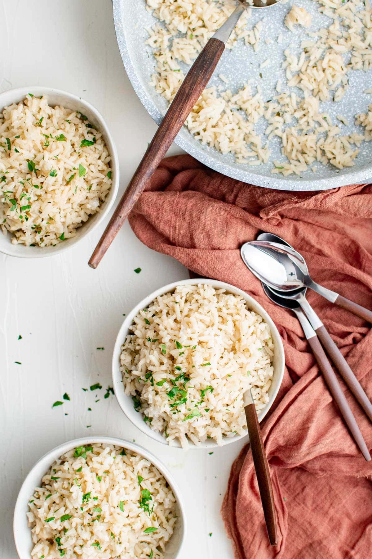 three white bowls of herb seasoned rice, pink napkin, spoons with wooden handles