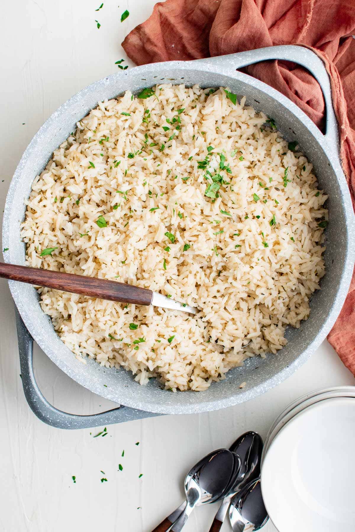 rice with herbs in a gray skillet with a wood handled spoon and a pink napkin