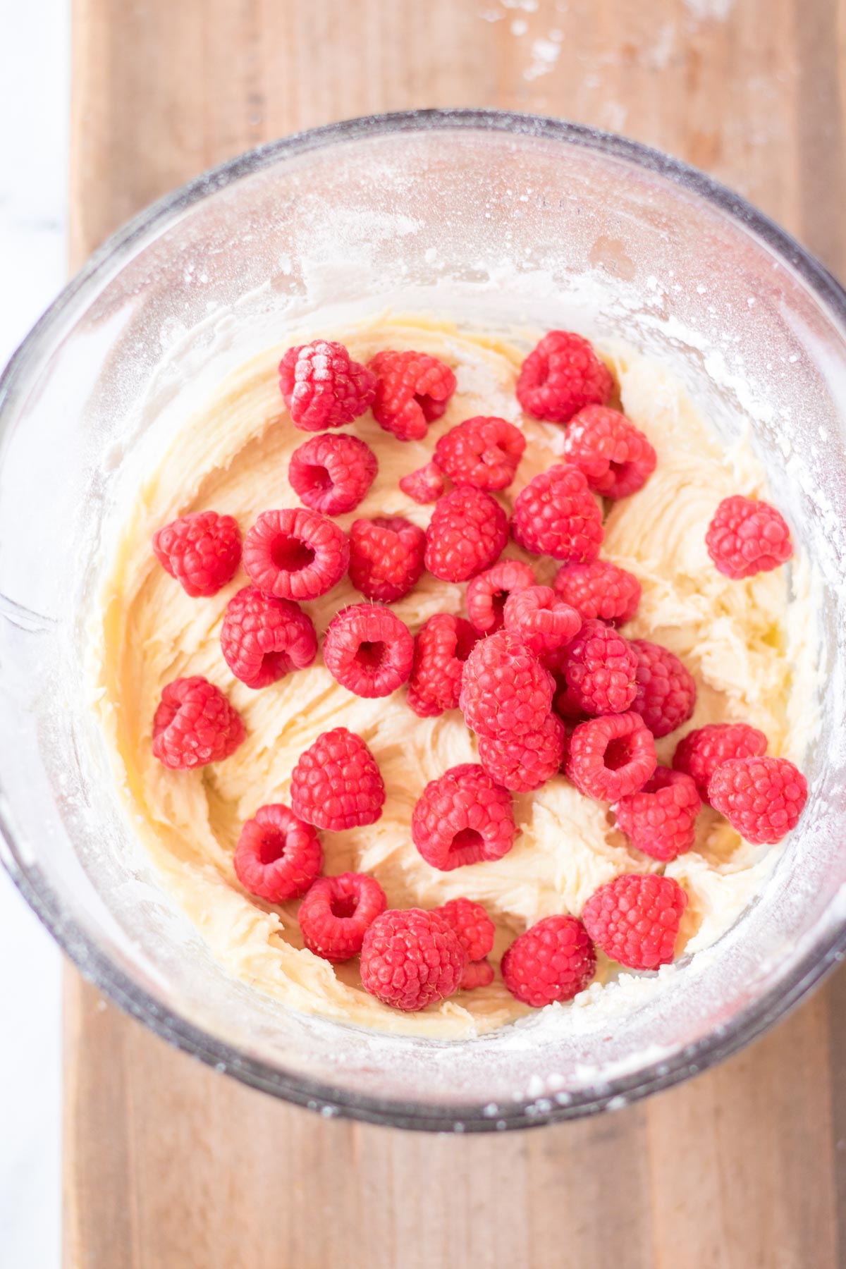muffin batter in a glass bowl with raspberries