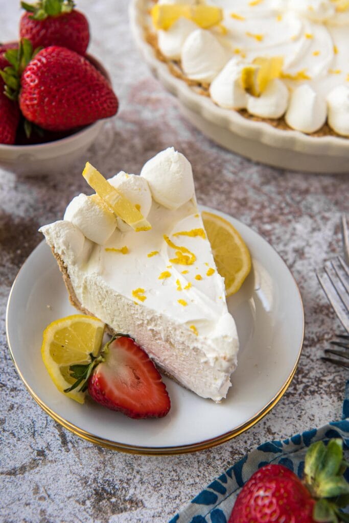 slice of no bake lemon cheesecake on a white plate, strawberries, lemon slices