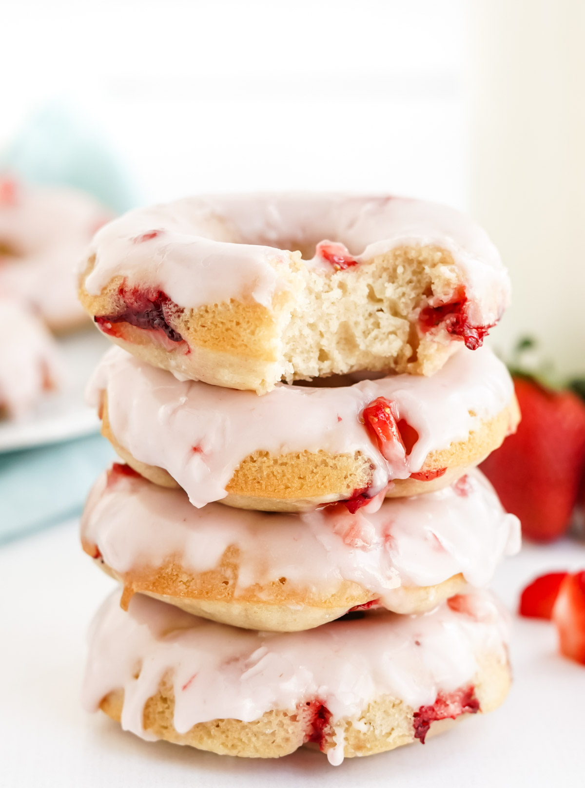 a stack of 4 strawberry doughnuts with dripping glaze with fresh strawberries 