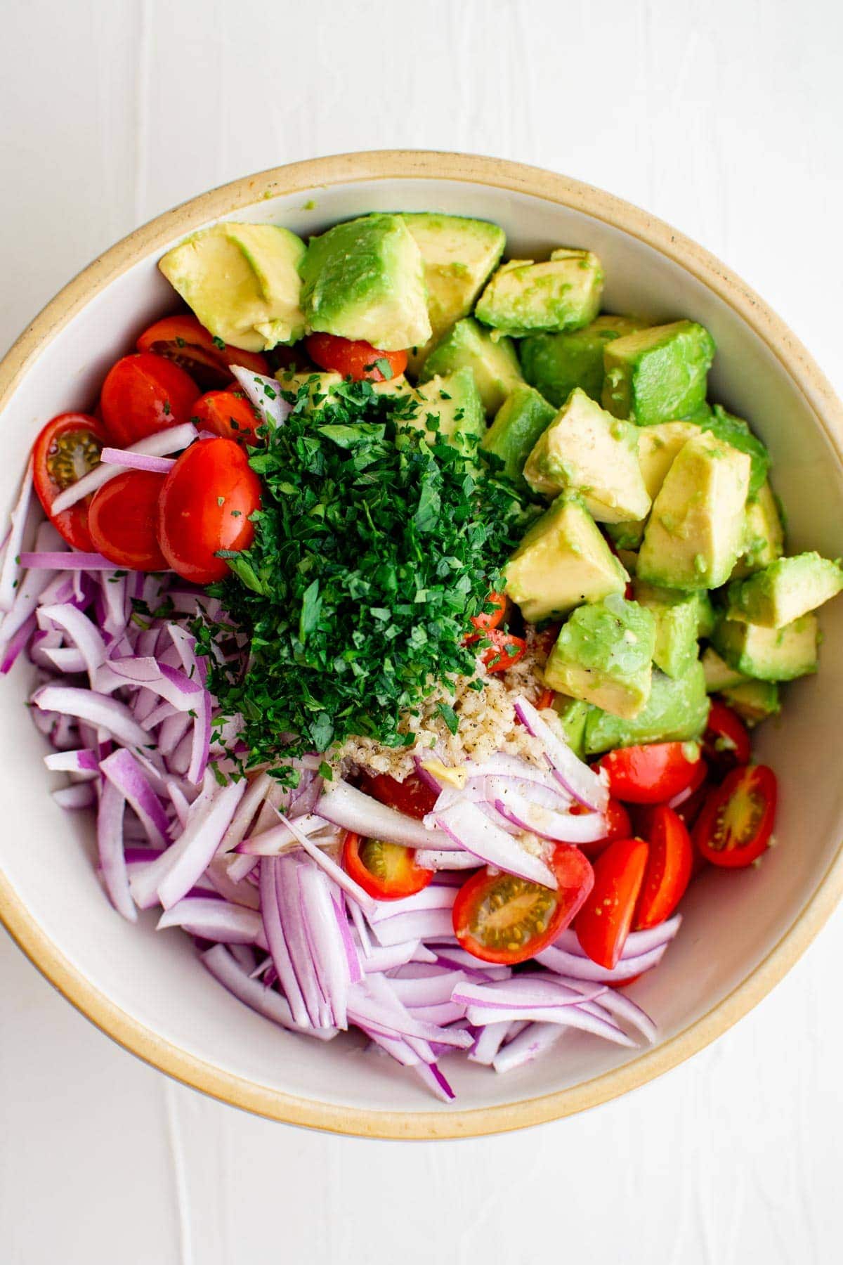 chopped avocados, tomatoes, parsley, sliced red onions in a white bowl