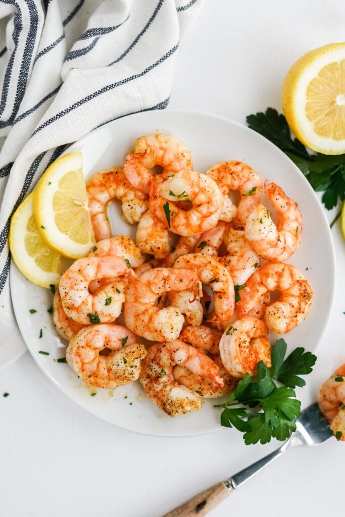 pink shrimp on a white plate with lemon slices, a fork and parsley