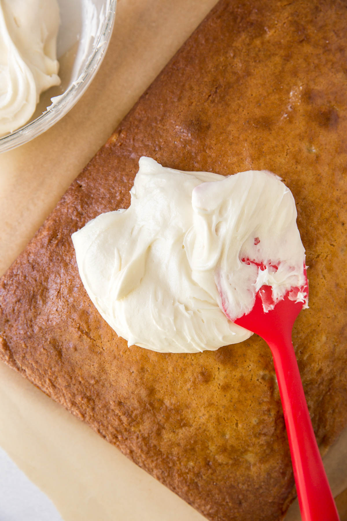 a glob of cream cheese frosting on top of a cake with a red spatula for spreading