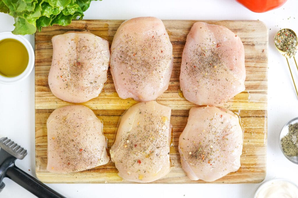 raw chicken breasts on a cutting board with seasoning