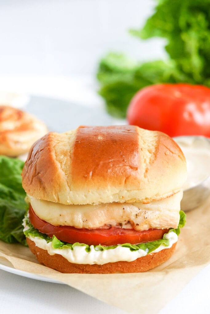 chicken sandwich on parchment paper, lettuce, tomatoes