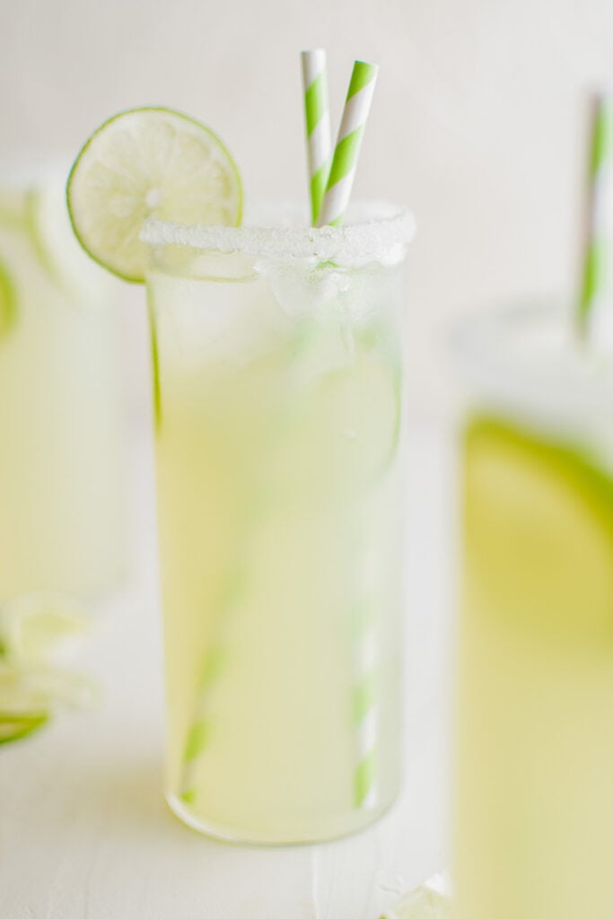 glass of limeade with a slice of lime and green straws