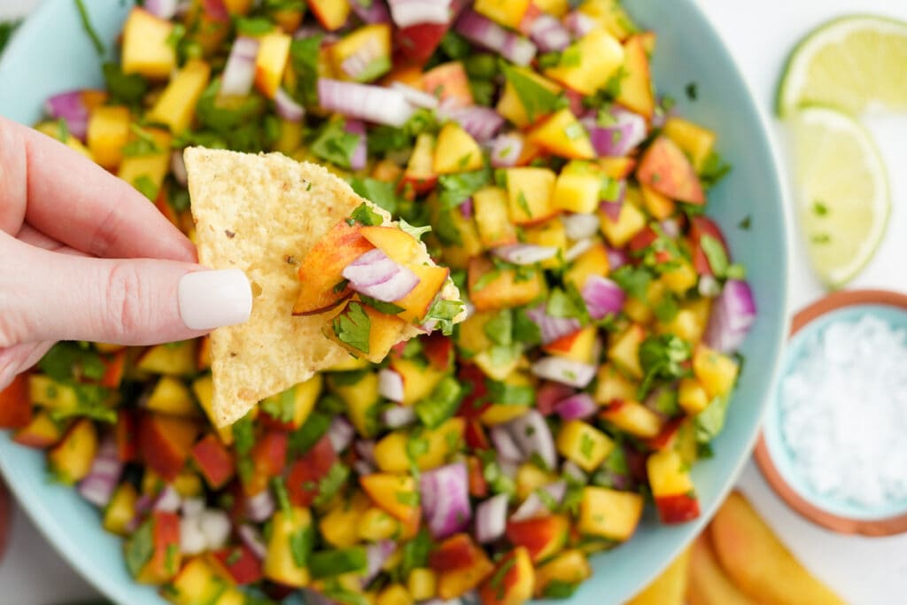 hand holding a chip dipped in peach salsa