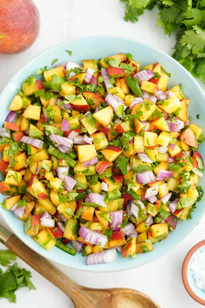large bowl full of peach salsa, wooden spoon