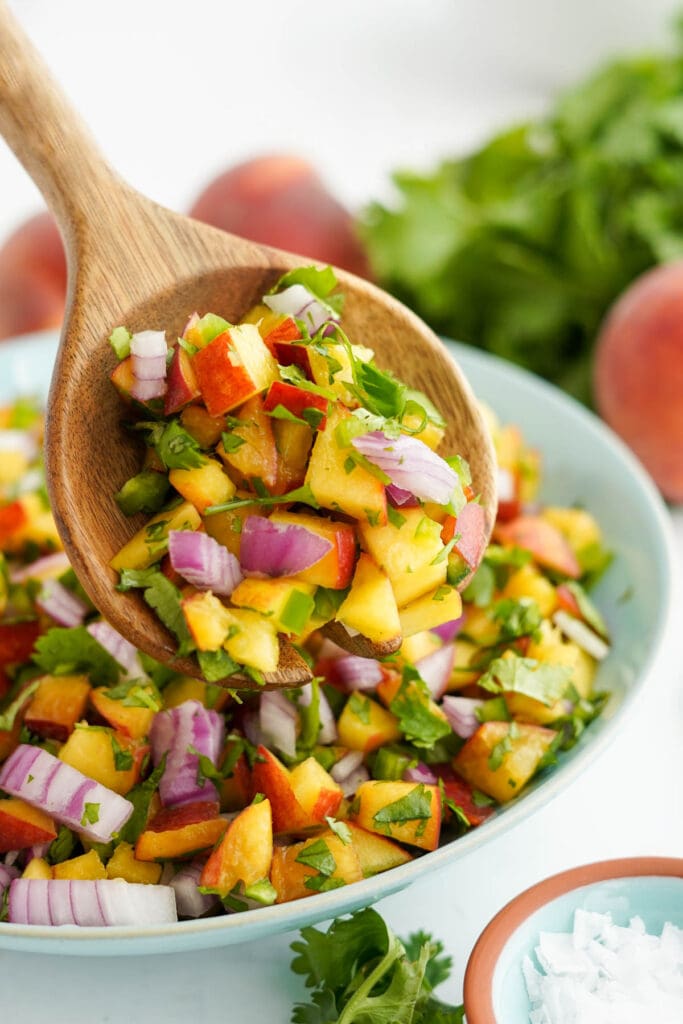 peach salsa in a bowl with a large wooden spoon