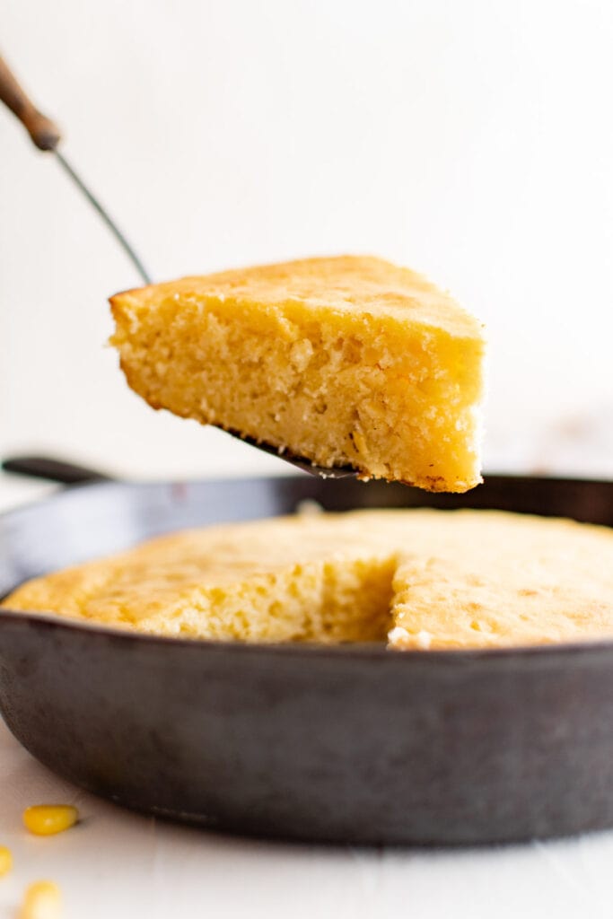 slice of sour ccream cornbread on a spatula above a cast iron skillet