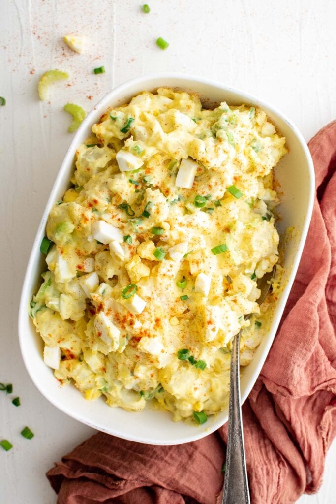 dish of southern potato salad with a large serving spoon, pink napkin