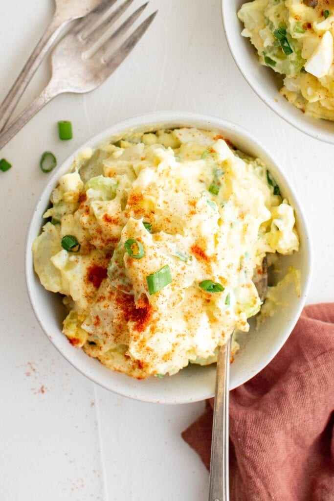 bowl of potato salad sprinkled with paprika, forks, pink napkin