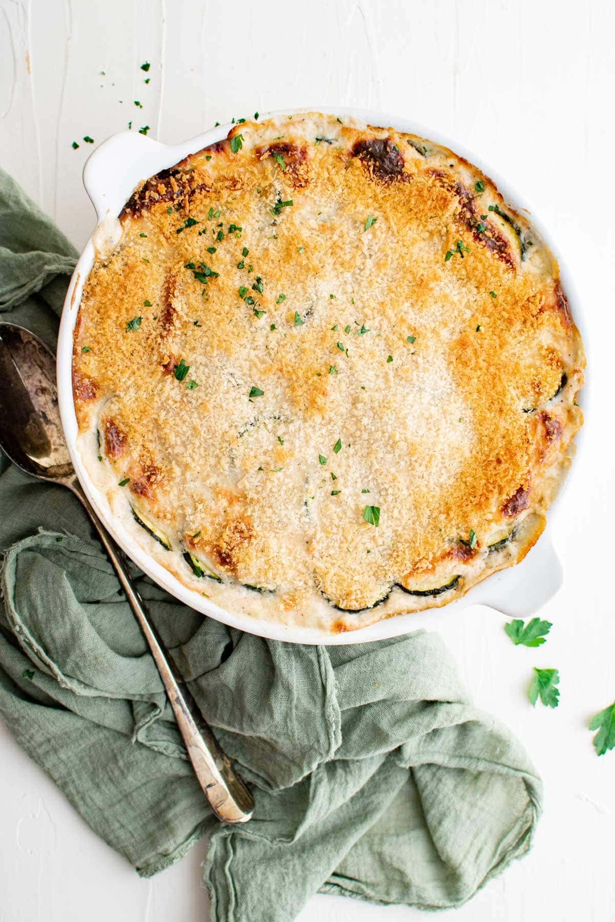 zucchini casserole in a white dish, green napkin, metal serving spoon