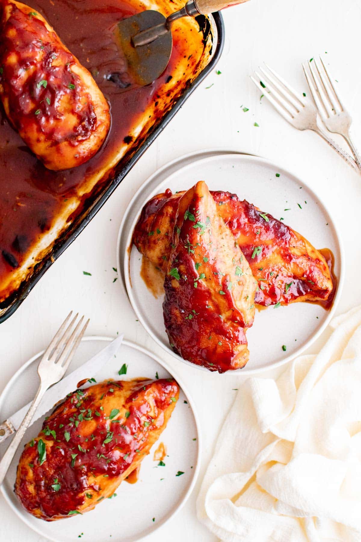 bbq chicken on white plates with a white napkin and forks