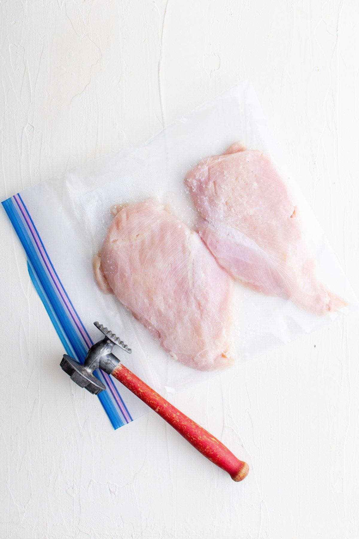 chicken breasts wrapped in plastic and a meat mallet