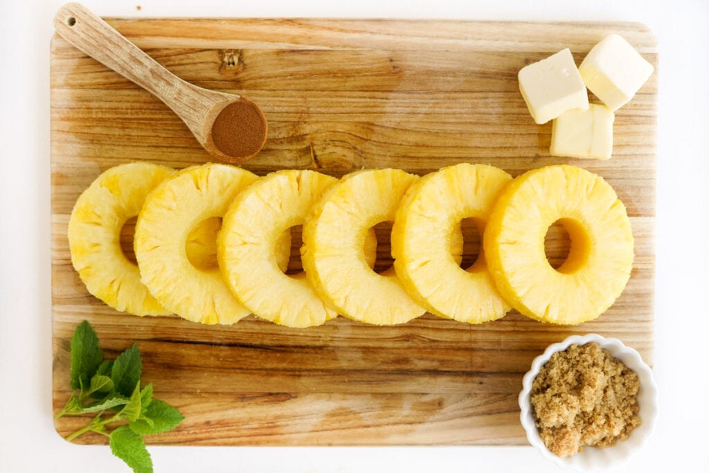 pineapple on a cutting board with dishes of sugar, butter and cinnamon