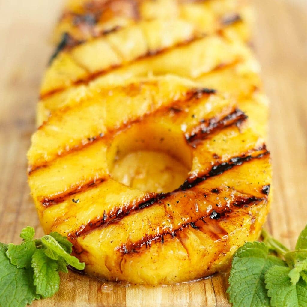 Slices of grilled pineapple on a wooden cutting board.