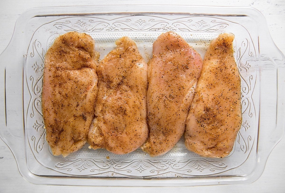 chicken breasts in a glass dish with seasoning