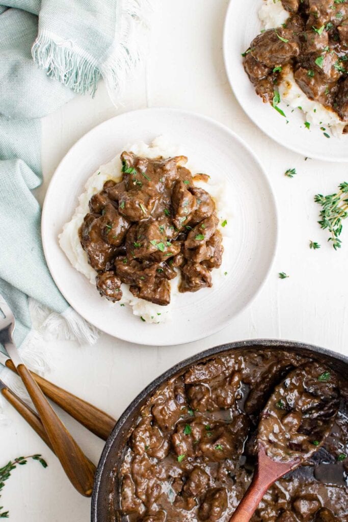 beef tips in gravy, over mashed potatoes on a plate.