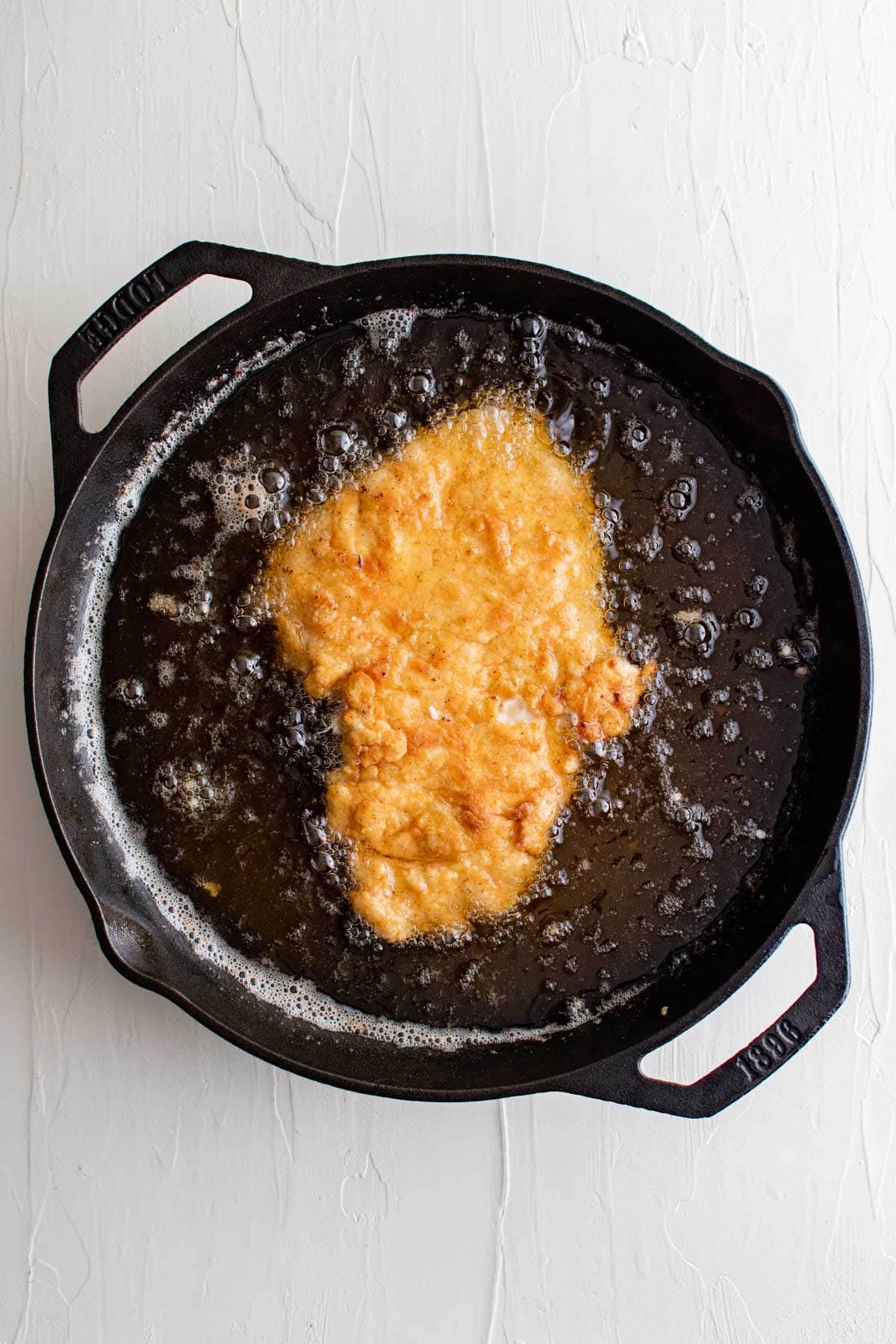 chicken breast frying in a cast iron skillet