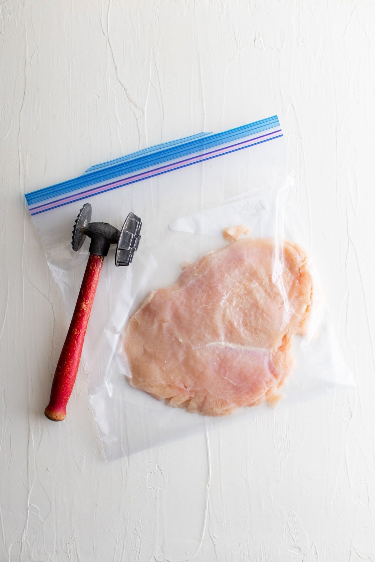 chicken breast in a plastic bag and a meat mallet