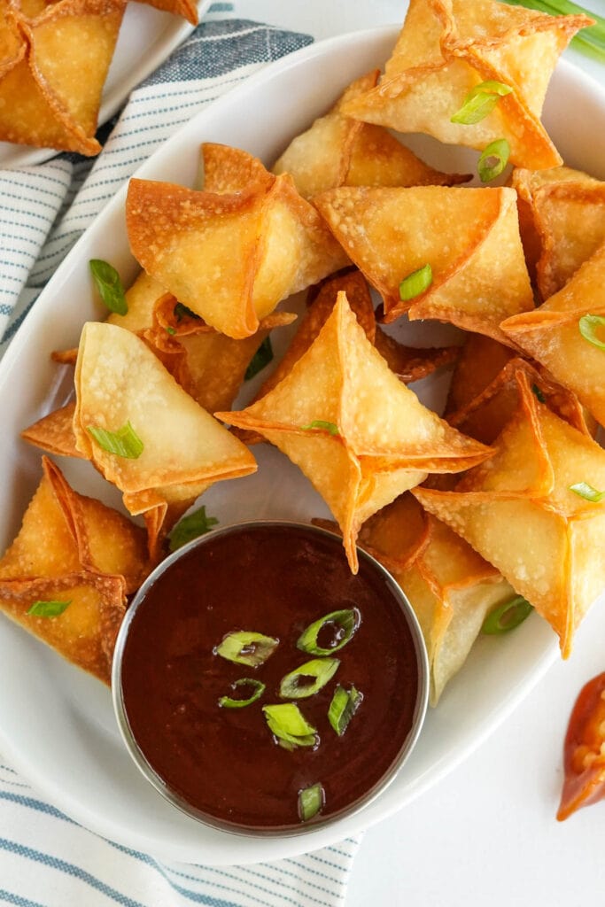 crab rangoon fried wontons on a white plate with a dipping sauce