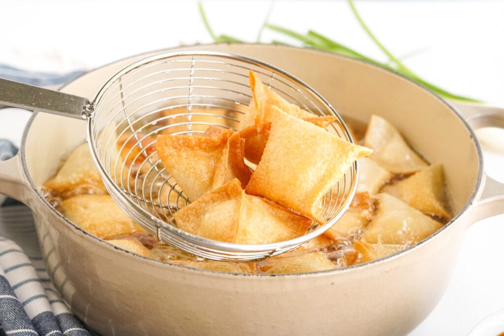 fried crab rangoon using a metal strainerand a pat of oil