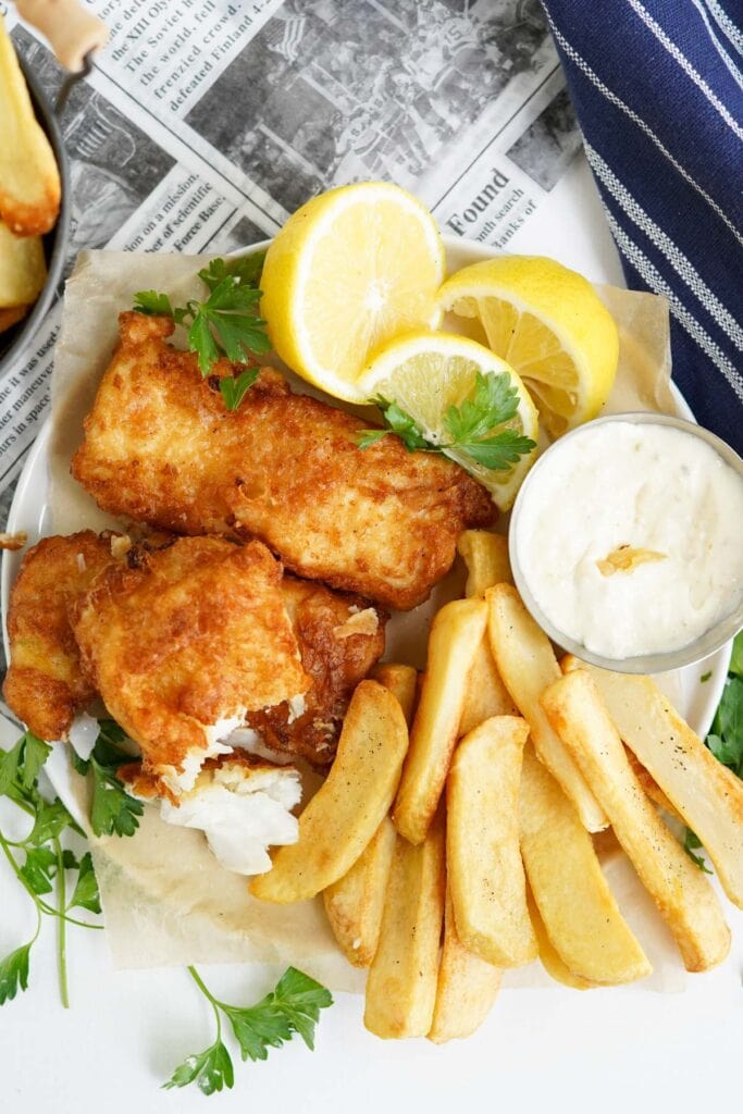 fried fish and chips in a basket with tartar sauce and lemons