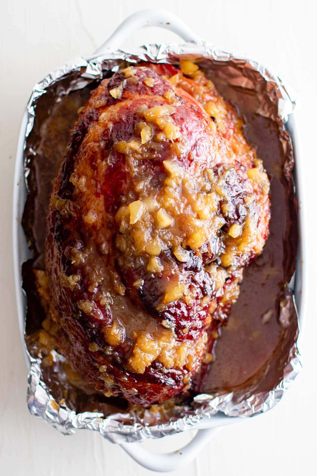 pineapple glazed ham in a baking dish with foil