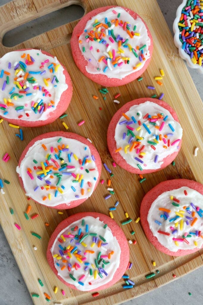 6 pink cookies on a wood background with frosting and sprinkles