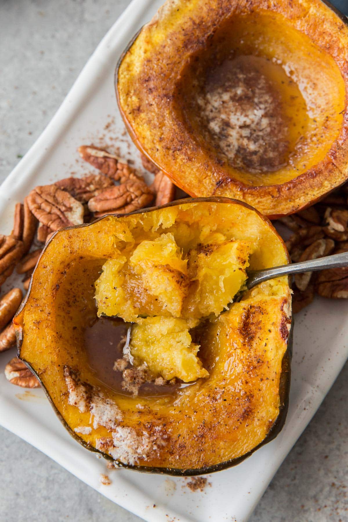baked acorn squash halves on a white platter, insides mashed with a fork