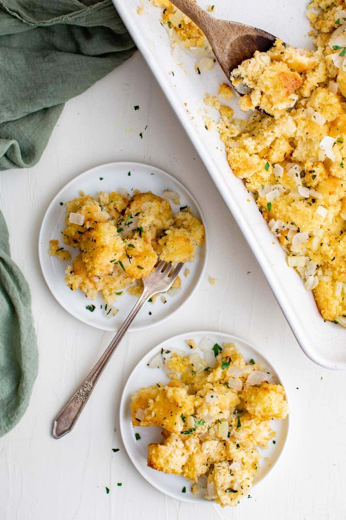 two plates with cornbread stuffing, a fork and green napkin