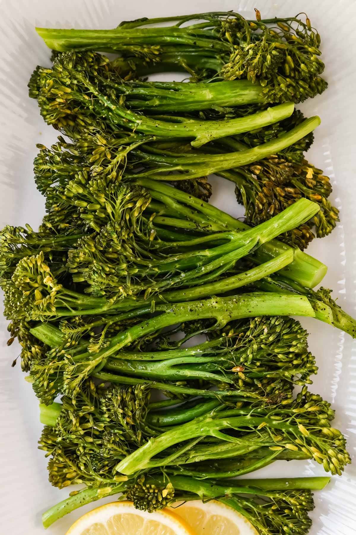 a large platter of roasted broccolini with lemon wedges