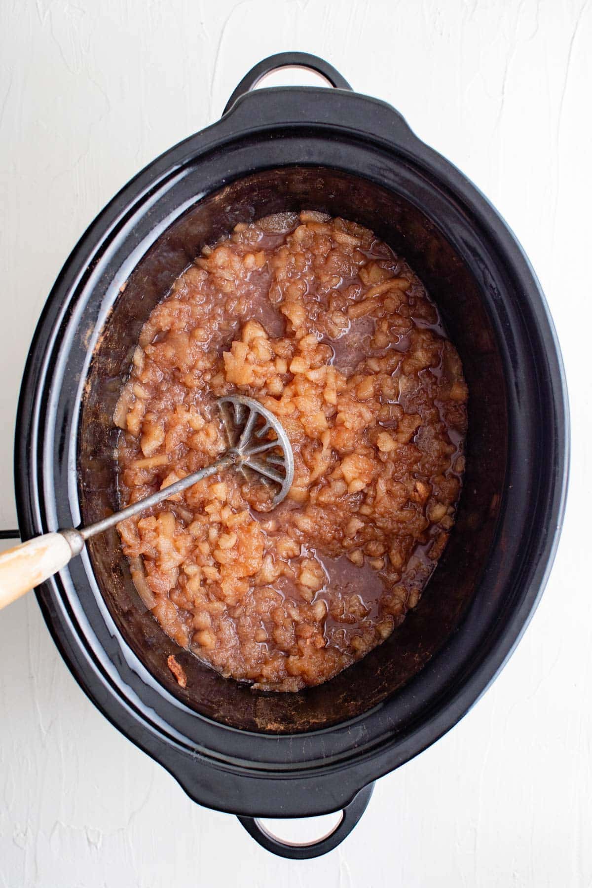masher and applesauce in slow cooker