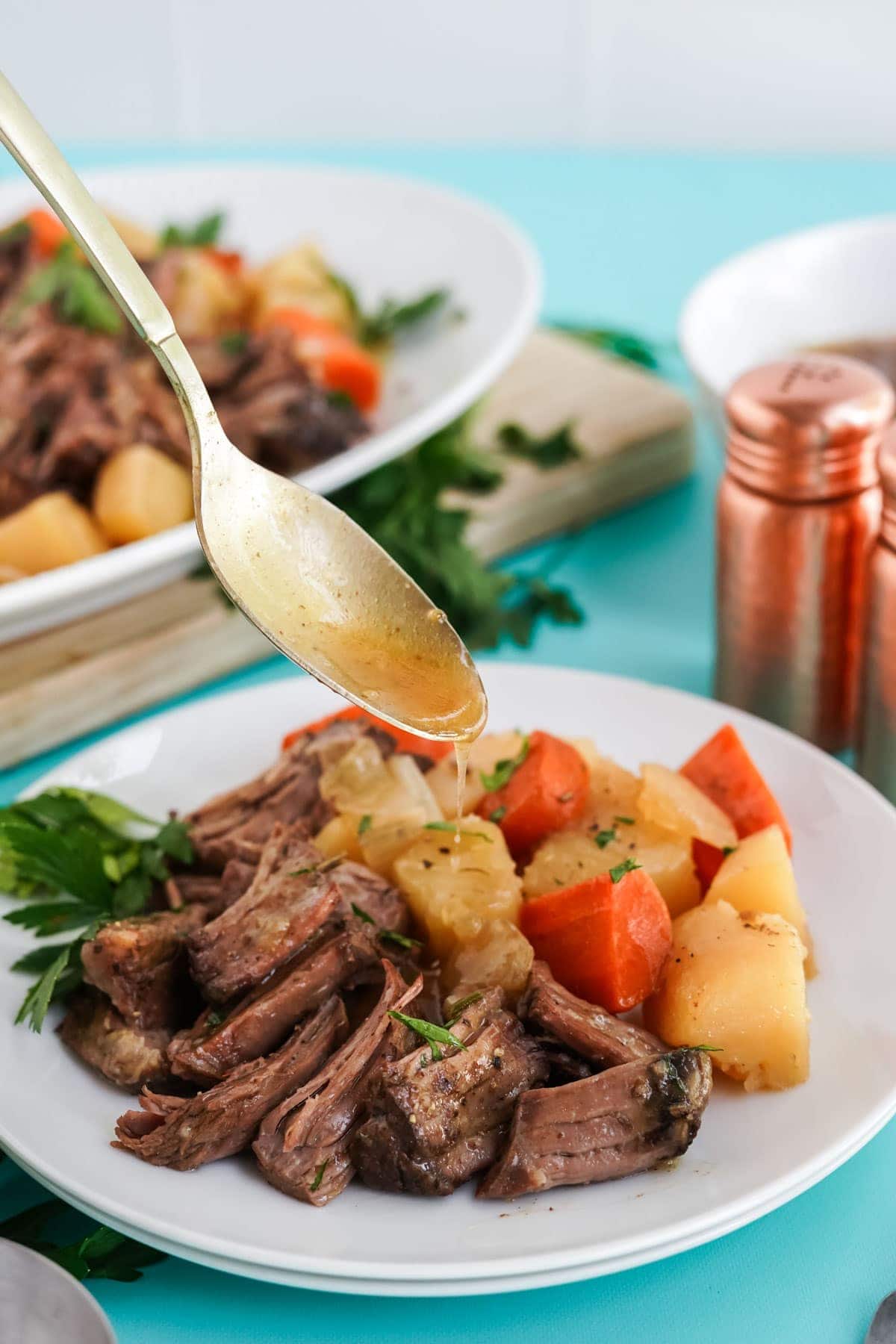 spooning gravy over pot roast on white plate