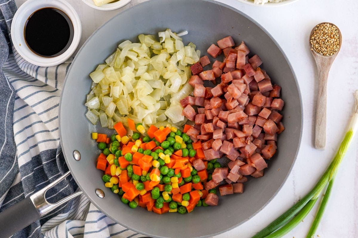 diced onions, ham, peas and carrots in a wok