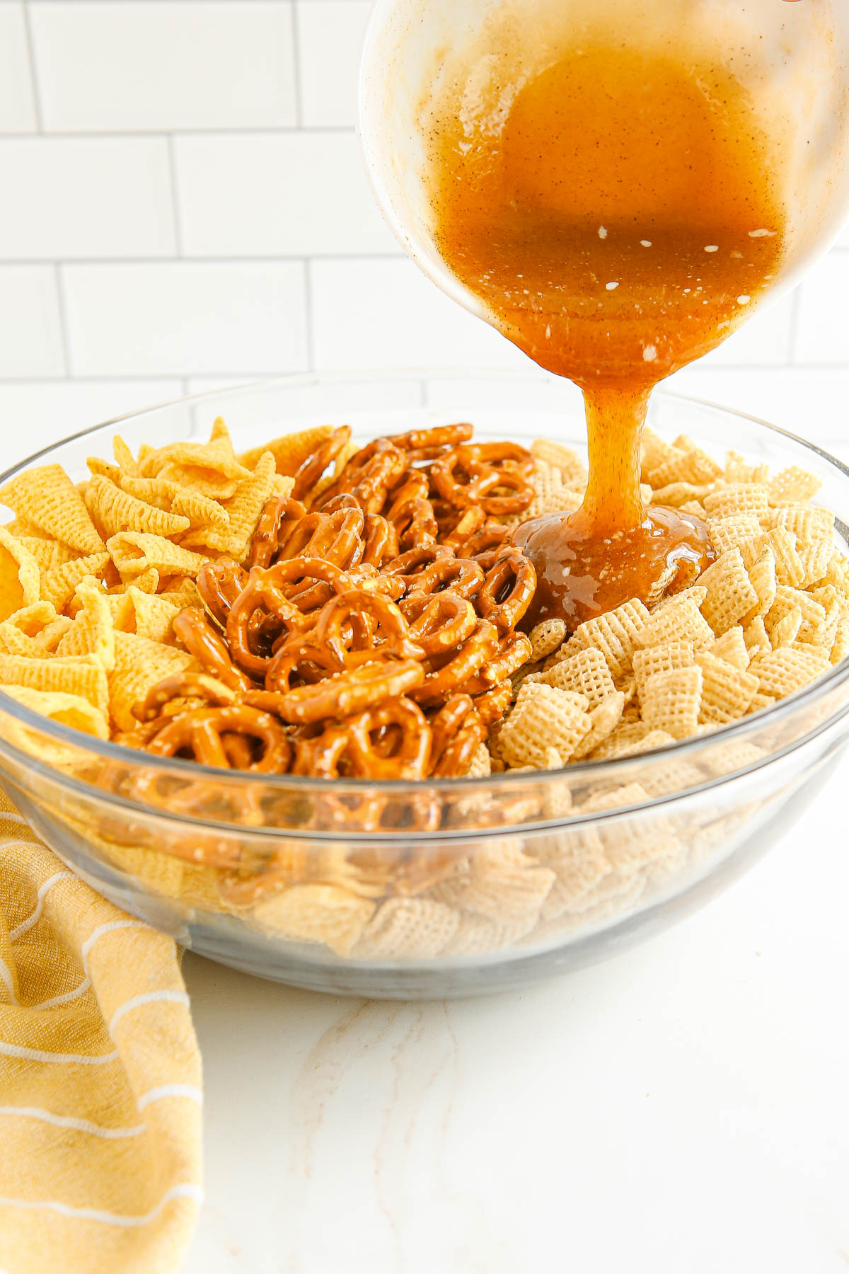 large glass bowl with bugles, pretzels and chex cereal, butter and brown sugar sauce pouring over